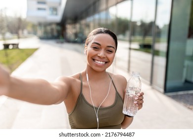 African American woman taking selfie with cellphone, recording video for her blog, holding water bottle on street. Black female influencer communicating to followers, making photo on outdoor training - Powered by Shutterstock