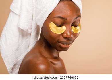 African American woman with towel and eye patches. Relaxing with eye patches, this woman enjoys skincare. Eye patches and towel for a soothing skincare routine. Black woman with skincare eye patches - Powered by Shutterstock