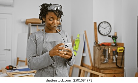 African american woman uses smartphone in woodworking workshop, surrounded by tools. - Powered by Shutterstock