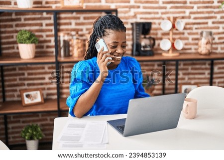 African american woman using laptop talking on smartphone at home