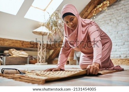 African American woman using Muslim prayer mat while praying at home.