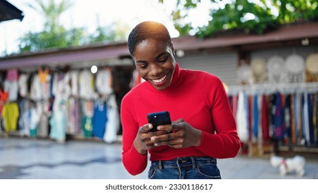 African american woman using smartphone smiling at street market - Shutterstock ID 2330118617