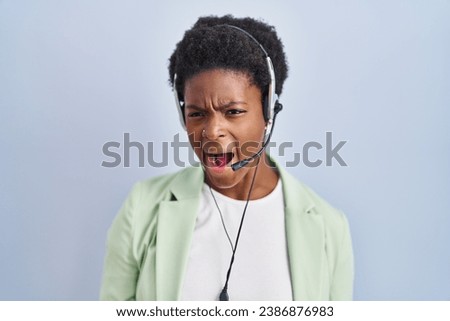 African american woman wearing call center agent headset angry and mad screaming frustrated and furious, shouting with anger. rage and aggressive concept. 