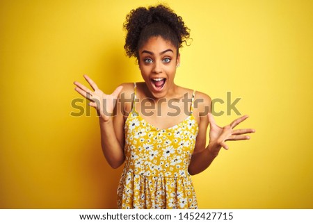 African american woman wearing casual floral dress standing over isolated yellow background celebrating crazy and amazed for success with arms raised and open eyes screaming excited. Winner concept