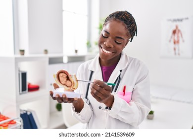 African american woman wearing doctor uniform holding anatomical model of uterus with fetus at clinic