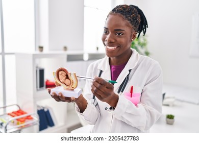 African american woman wearing doctor uniform holding anatomical model of uterus with fetus at clinic - Powered by Shutterstock