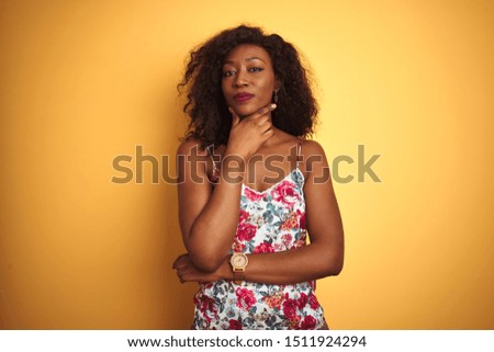 African american woman wearing floral summer t-shirt over isolated yellow background looking confident at the camera with smile with crossed arms and hand raised on chin. Thinking positive.