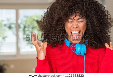 African american woman wearing headphones celebrating mad and crazy for success with arms raised and closed eyes screaming excited. Winner concept