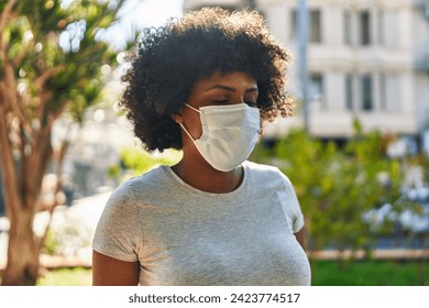 African american woman wearing medical mask standing at park - Powered by Shutterstock