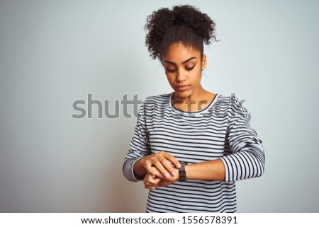 African american woman wearing navy striped t-shirt standing over isolated white background Checking the time on wrist watch, relaxed and confident