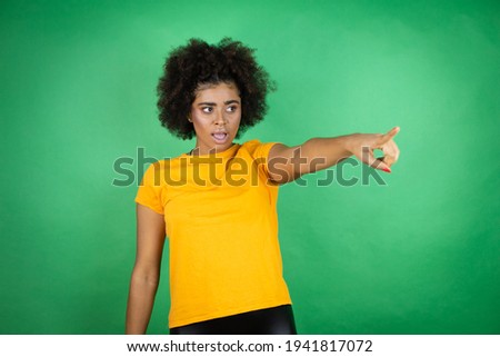 African american woman wearing orange casual shirt over green background pointing with finger surprised ahead, open mouth amazed expression, something on the front