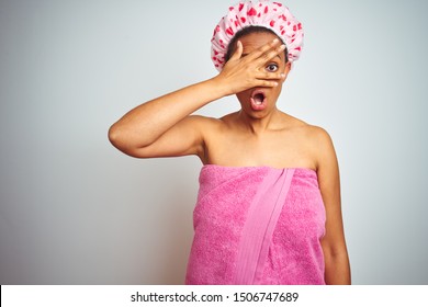 African American Woman Wearing Pink Shower Towel After Bath Over Isolated Background Peeking In Shock Covering Face And Eyes With Hand, Looking Through Fingers With Embarrassed Expression.