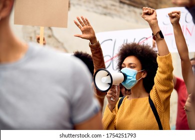 African American woman wearing protective face mask  while shouting through megaphone in solidarity with the Black Lives Matter movement. - Shutterstock ID 1754251793