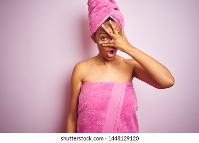 African American Woman Wearing Shower Towel After Bath Over Pink Isolated Background Peeking In Shock Covering Face And Eyes With Hand, Looking Through Fingers With Embarrassed Expression.