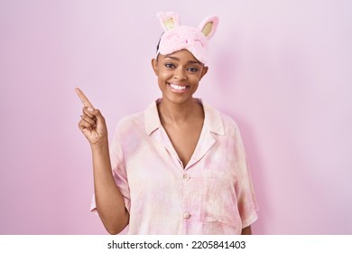 African american woman wearing sleep mask and pajama smiling happy pointing with hand and finger to the side  - Shutterstock ID 2205841403
