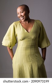 African American woman wearing summer dress happy face smiling with arms in pockets looking down. positive person