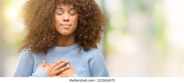 African american woman wearing a sweater smiling with hands on chest with closed eyes and grateful gesture on face. Health concept.
