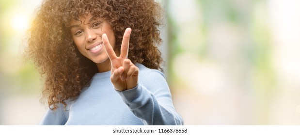 African American Woman Wearing A Sweater Smiling Looking To The Camera Showing Fingers Doing Victory Sign. Number Two.