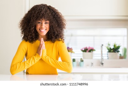 African American Woman Wearing Yellow Sweater At Kitchen Praying With Hands Together Asking For Forgiveness Smiling Confident.