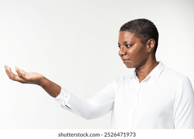 African American woman in white shirt extends hand, looking thoughtful. Woman with thoughtful expression, hand extended. Neutral background, white shirt, thoughtful gaze of woman. - Powered by Shutterstock