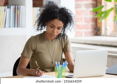 African American Woman Worker Or Student Studying Working With Laptop Holding Pen Making Notes, Focused Young Black Lady Writing Down Information Doing Online Research Paperwork At Office Workplace