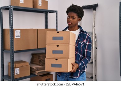 African American Woman Working At Small Business Ecommerce Holding Boxes Clueless And Confused Expression. Doubt Concept. 