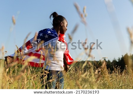 African american woman wrapped in american flag flutters waving in the wind. Happy 4th of July! Independence Day celebrating. Stars and stripes. Freedom concept.
