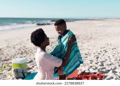 African american woman wrapping towel around wet son while spending leisure time at beach under sky. Copy space, unaltered, family, together, childhood, care, nature, vacation, enjoyment and summer. - Powered by Shutterstock