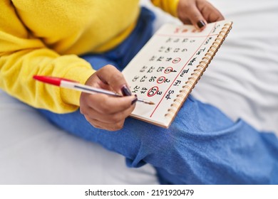 African American Woman Writing On Calendar Sitting On Bed At Bedroom