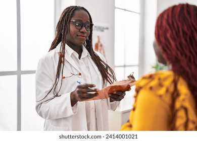 African american women doctor and patient having consultation writing medical report at clinic - Powered by Shutterstock