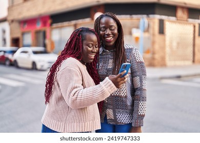 African american women friends smiling confident using smartphone at street - Powered by Shutterstock