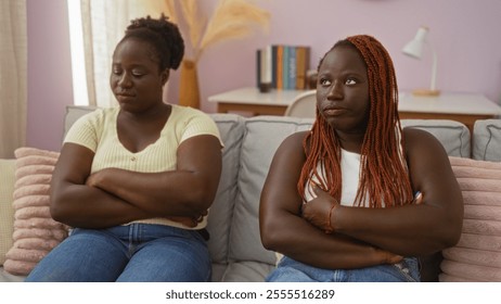 African american women sitting in a living room with crossed arms, looking thoughtful and emotional in an indoor home setting. - Powered by Shutterstock