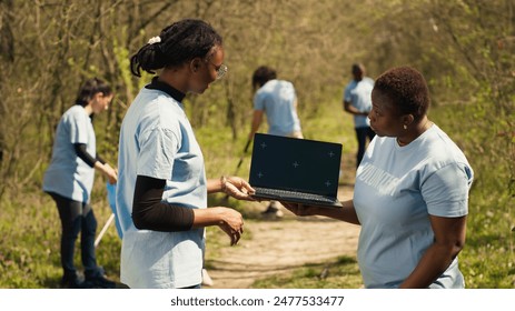 African american women use laptop with greenscreen during a litter cleanup activity to protect the environment and preserve nature. Volunteers cleaning up trash, ecological justice. Camera A. - Powered by Shutterstock