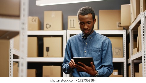 African American Worker With Computer Doing Registration In Delivery Room Full Of Boxes.