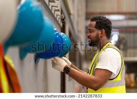 African American worker is hanging his safety helmet on the rack inside the heavy industrial factory for protection and accident prevention