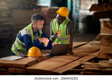 African American Worker And His Colleagues Using Laptop While Drinking Coffee And Working At Wood Warehouse. 
