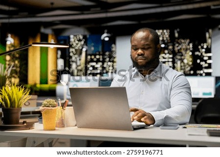 African american worker proofreading a document before transcribing on notebook, extracting the main ideas from reports on laptop. Expert documenting after hours late at night.