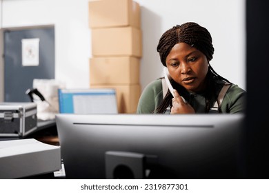 African american worker talking at landline phone with remote client discussing delivery details in storehouse. Storage room employee checking online orders on computer in warehouse - Powered by Shutterstock