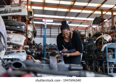 African American Worker Woman Wear Spectacles Make A Note Of The Product List On Clipboard In Factory Auto Parts. Female Employee Business Warehouse Motor Vehicle.