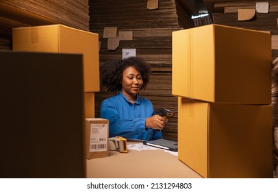 African American worker  working in storage, taking parcel and scanning barcode, putting box on shelf. Female business person at workplace in warehouse, concept of delivering and logistics.  
