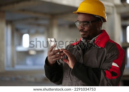 African american workman in yellow hard hat with smartphone stands at construction site. Worker holds in hands smartphone and smiles Stock fotó © 