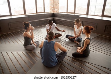 African american yoga instructor talking to diverse group sitting on mat in studio, multiracial happy people having conversation about healthy mindful life and motivation at training seminar class - Powered by Shutterstock