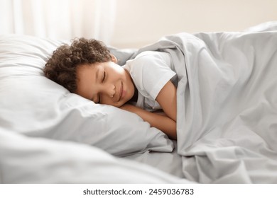 African American young boy peacefully sleeps in a bed, with his body curled up and his eyes closed. The room is dimly lit, and a blanket covers him. - Powered by Shutterstock