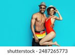 African American young couple wearing swimwear and hats, posing against a bright blue background. They both appear happy and relaxed, enjoying the summer weather.