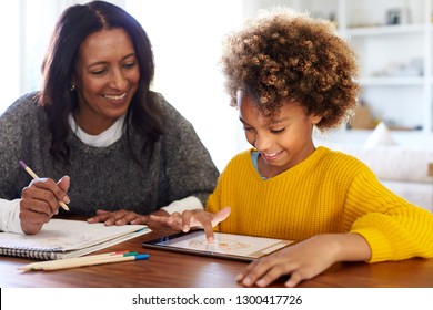 African American young grandmother sitting at table doing homework with her granddaughter using a tablet computer, close up