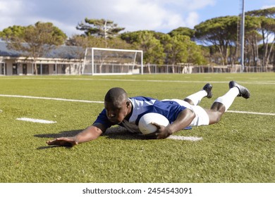 African American young male athlete scoring a try a rugby ball on a field. He wears a blue jersey, white shorts, and has short black hair. - Powered by Shutterstock