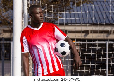 African American young male athlete holding soccer ball, standing by goal post, copy space. Wearing red and white jersey, looking focused, with short black hair, unaltered - Powered by Shutterstock