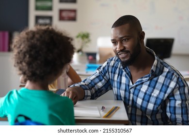 African american young male teacher talking on african american elementary schoolboy sitting at desk. unaltered, education, communication, childhood, occupation, teaching and school concept. - Powered by Shutterstock