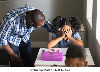 African American Young Male Teacher Consoling Sad Biracial Elementary Schoolgirl Sitting At Desk. Unaltered, Education, Communication, Childhood, Sadness, Depression, Failure And School Concept.