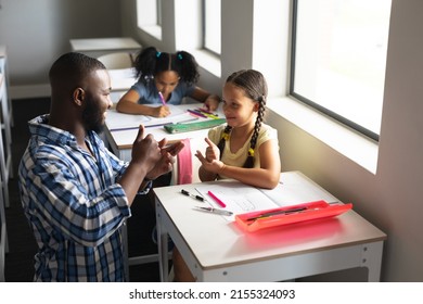 African american young male teacher communicating in sign language with caucasian elementary girl. unaltered, education, childhood, learning, teaching, disability and school concept. - Shutterstock ID 2155324093